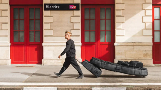 Surfer walking down the street pulling his wheeled DB Coffin surfboard travel bag.