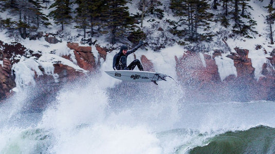 A surfer performing an aerial while wearing the Xcel Drylock 5/4 hooded wetsuit.